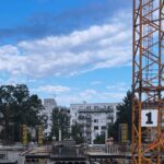 Rozestavěná budova s věžovým jeřábem v městské zástavbě.