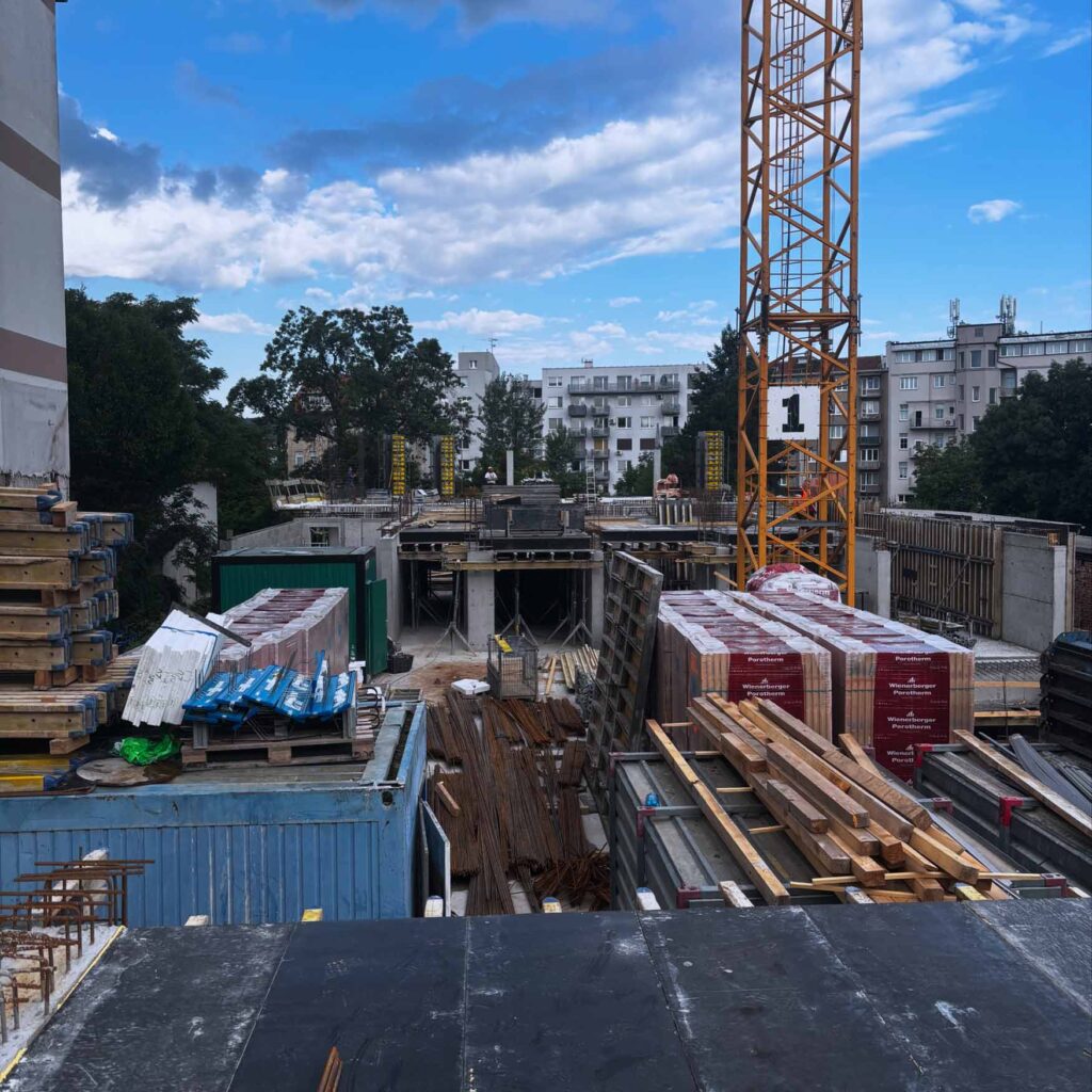 Staveniště bytového domu s jeřábem a stavebním materiálem.