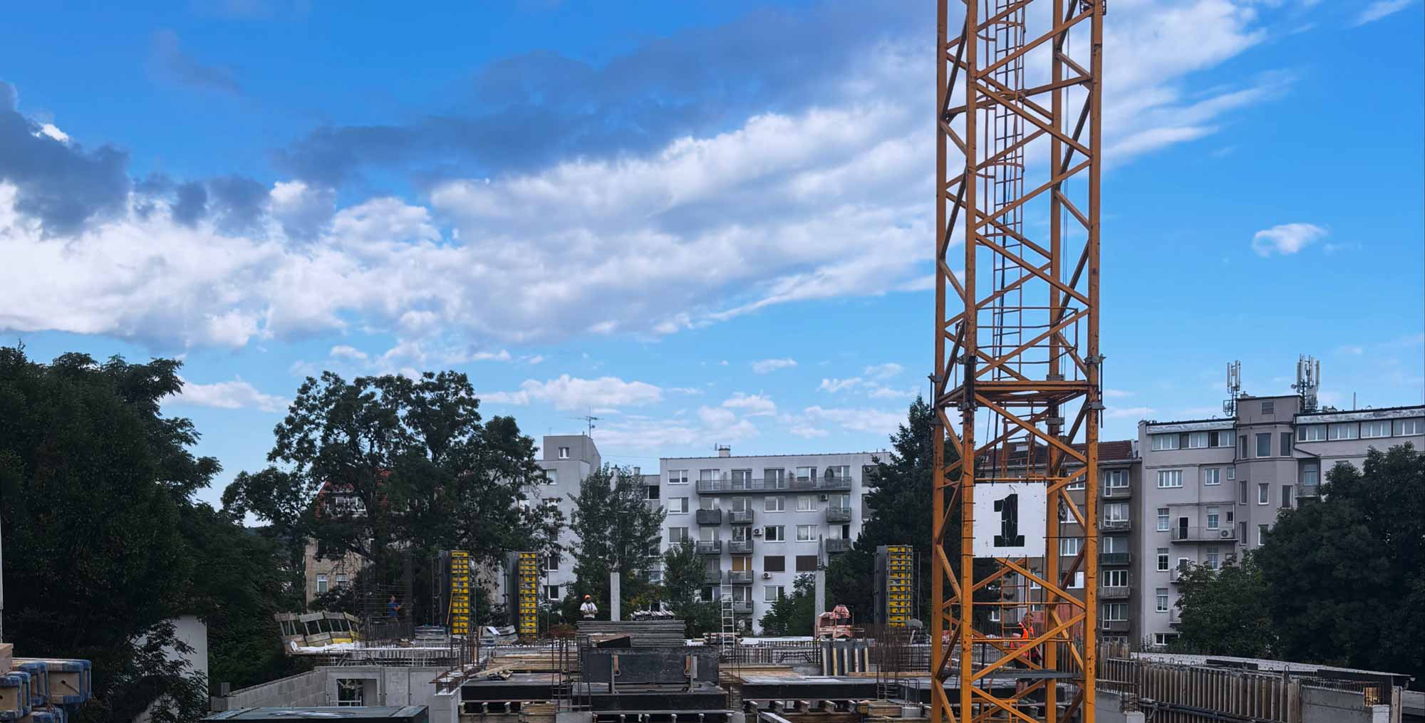 Rozestavěná budova s věžovým jeřábem v městské zástavbě.