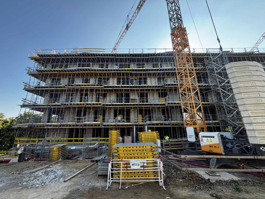 Vícepodlažní budova ve výstavbě s lešením a věžovým jeřábem.